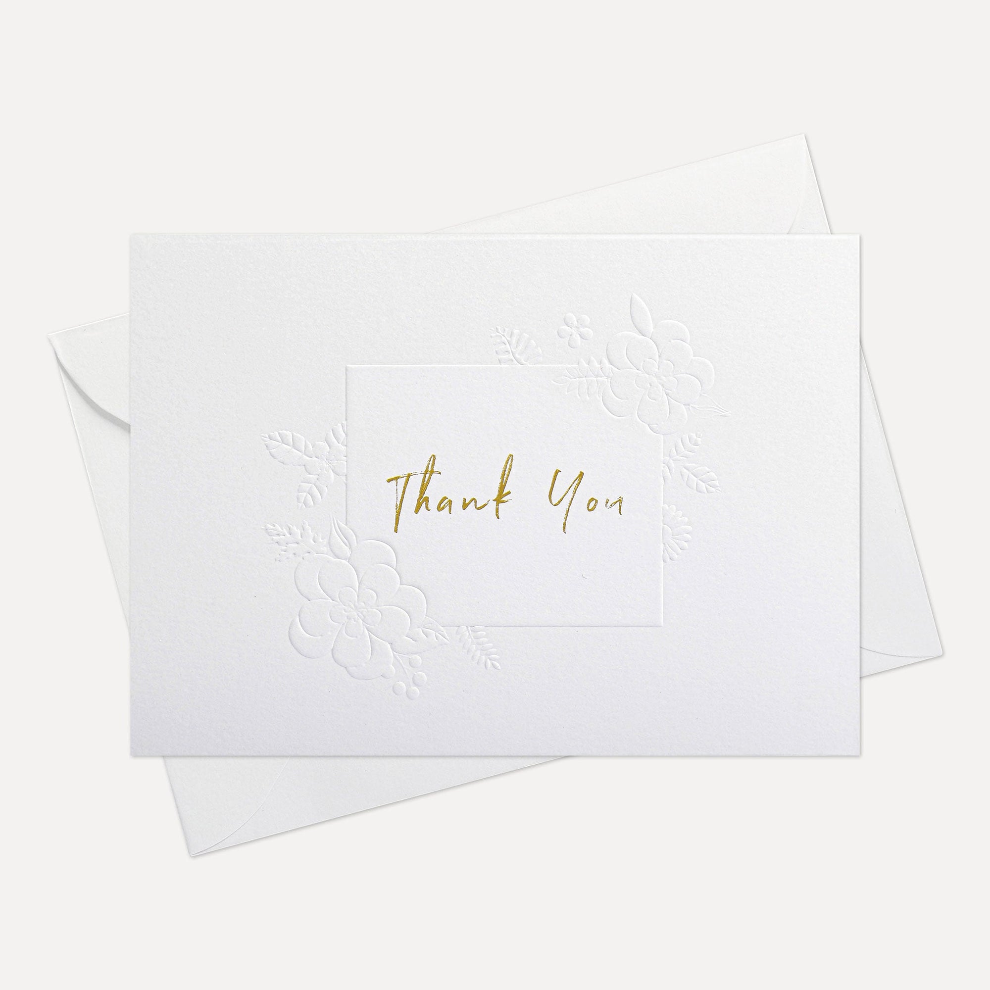 Overhead view of a minimalist luxury white thank you card featuring gold text and an elegant debossed floral border, displayed with its matching white envelope.