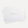 Overhead view of a minimalist luxury white thank you card featuring gold text and an elegant debossed floral border, displayed with its matching white envelope.