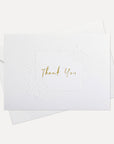 Overhead view of a minimalist luxury white thank you card featuring gold text and an elegant debossed floral border, displayed with its matching white envelope.