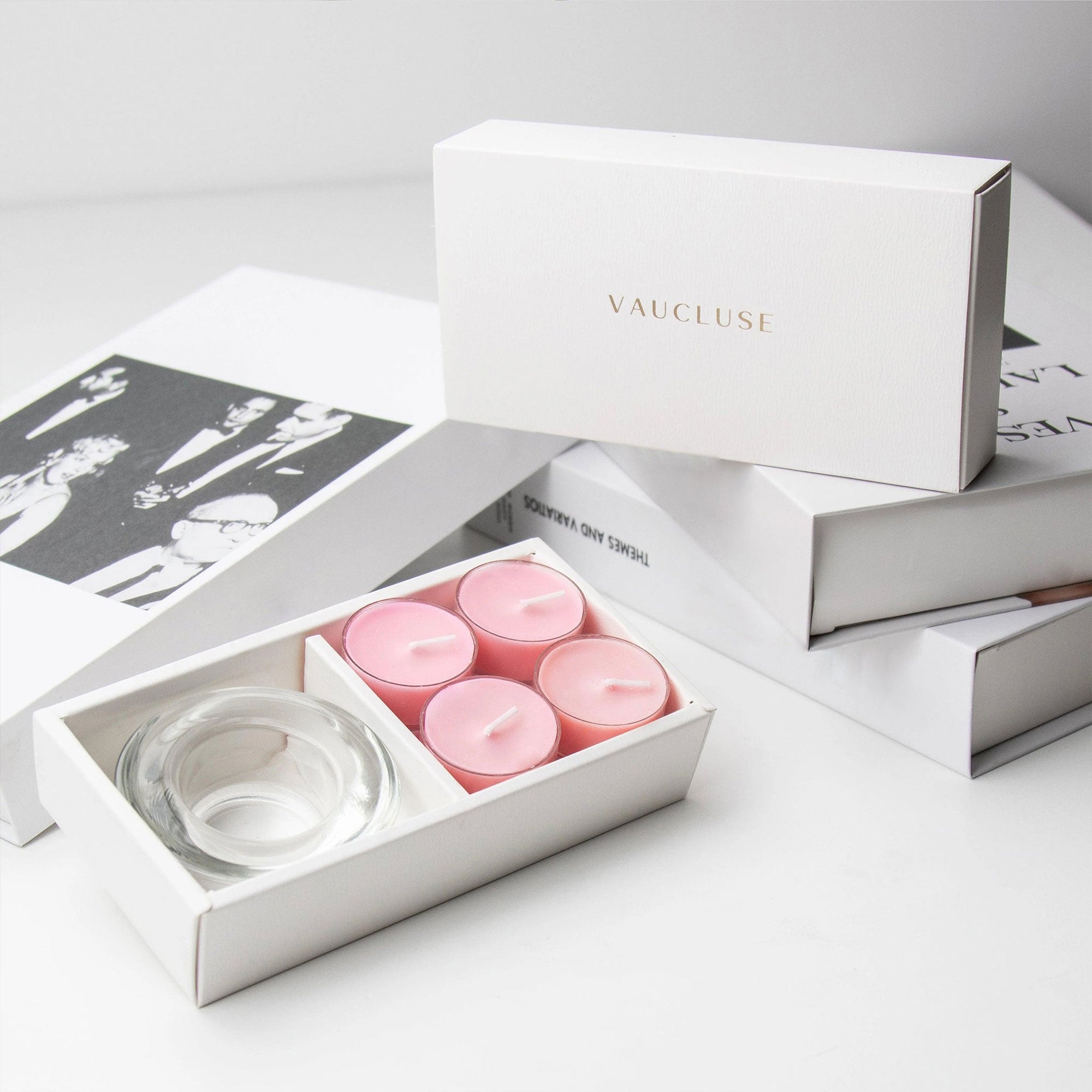 Luxury retail unboxing display showing the open pink rose candle holder set resting against stacked white gift boxes with gold foil branding.