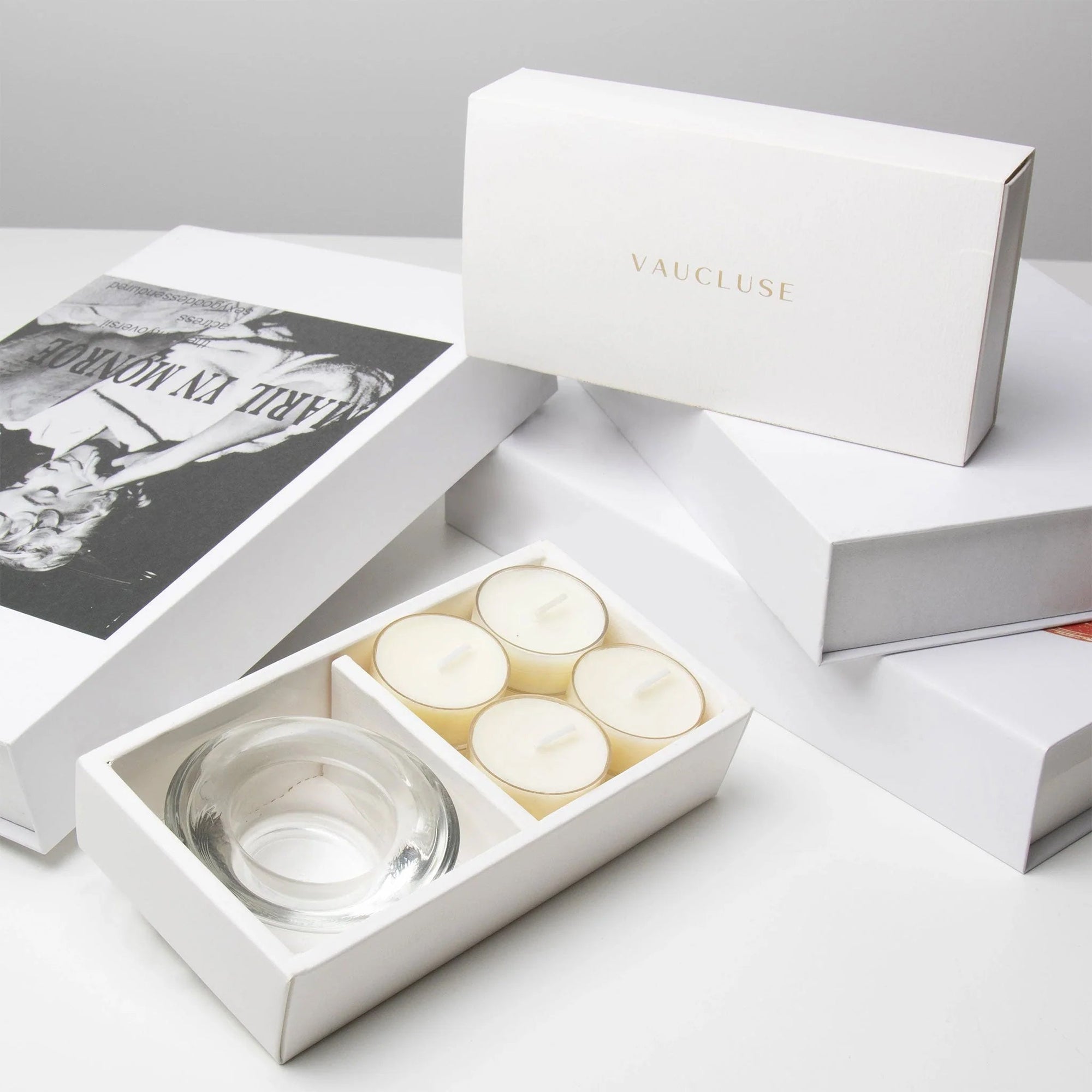 Elegant aesthetic unboxing display featuring the open vanilla tealight set next to stacked luxury white gift boxes with gold branding.