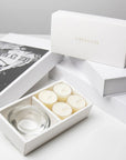 Elegant aesthetic unboxing display featuring the open vanilla tealight set next to stacked luxury white gift boxes with gold branding.