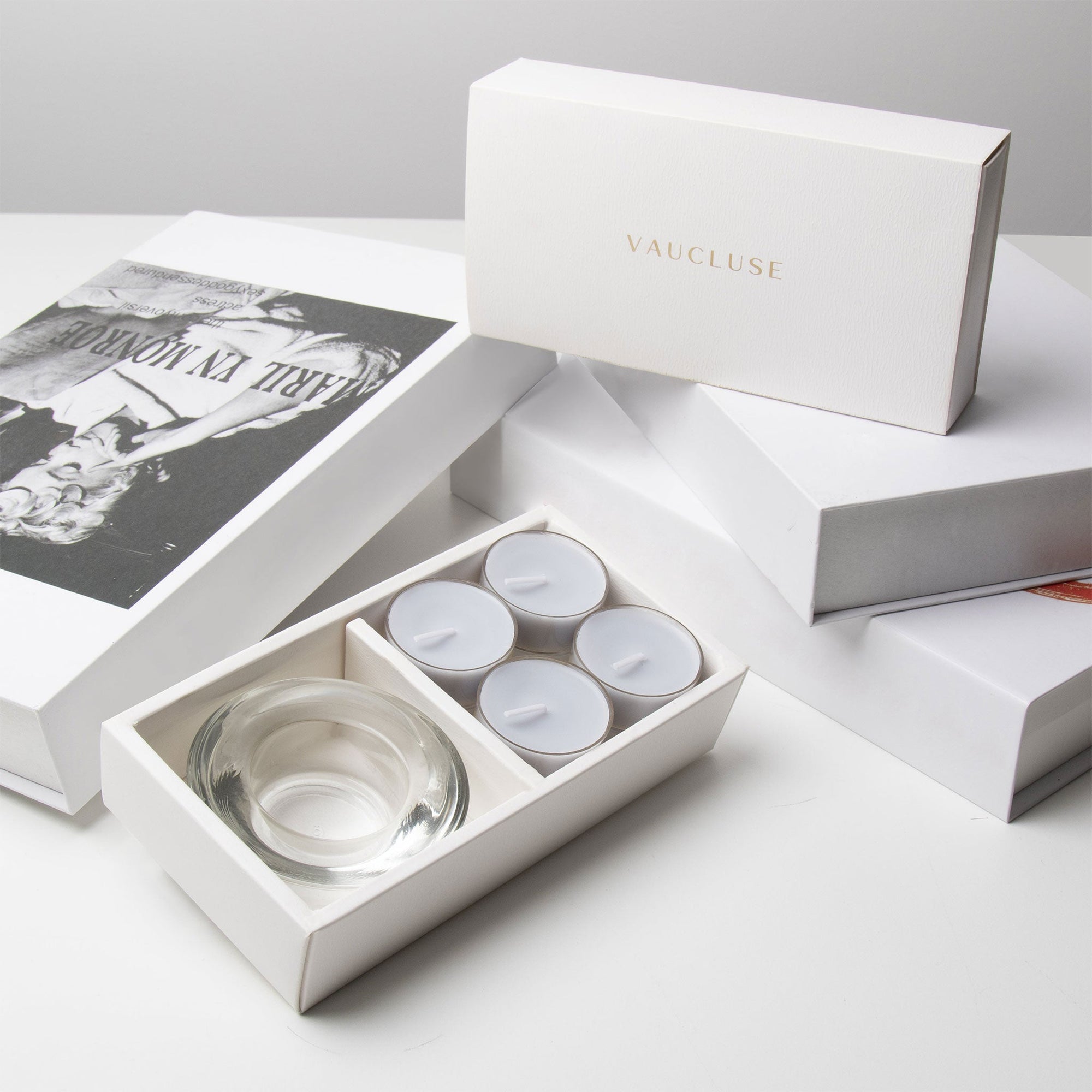 Luxury retail unboxing display showing the open grey velvet candle holder set resting against stacked premium gift boxes with gold branding.