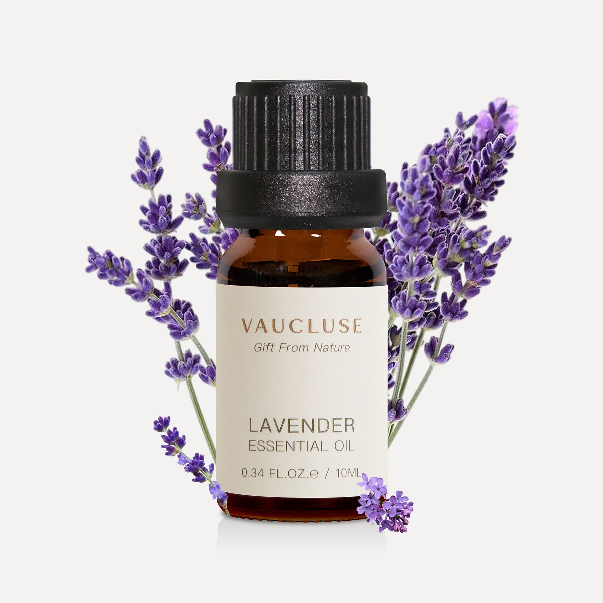 A 10ml amber glass bottle of Vaucluse Lavender Essential Oil accented with fresh purple lavender flower sprigs in the background.