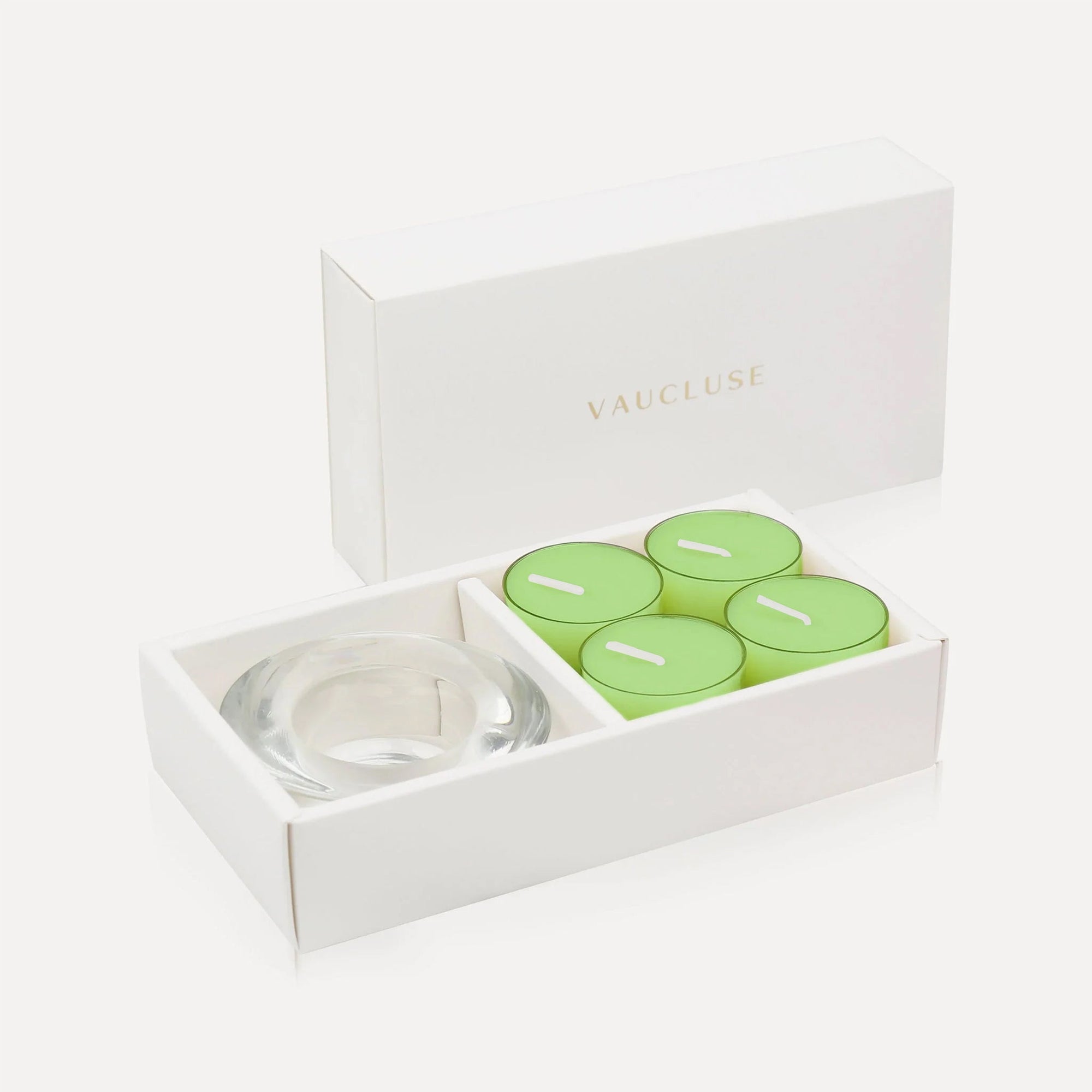 An open luxury white gift box cleanly displaying a set of four vibrant green lily tealight candles alongside a thick round clear glass candle holder.