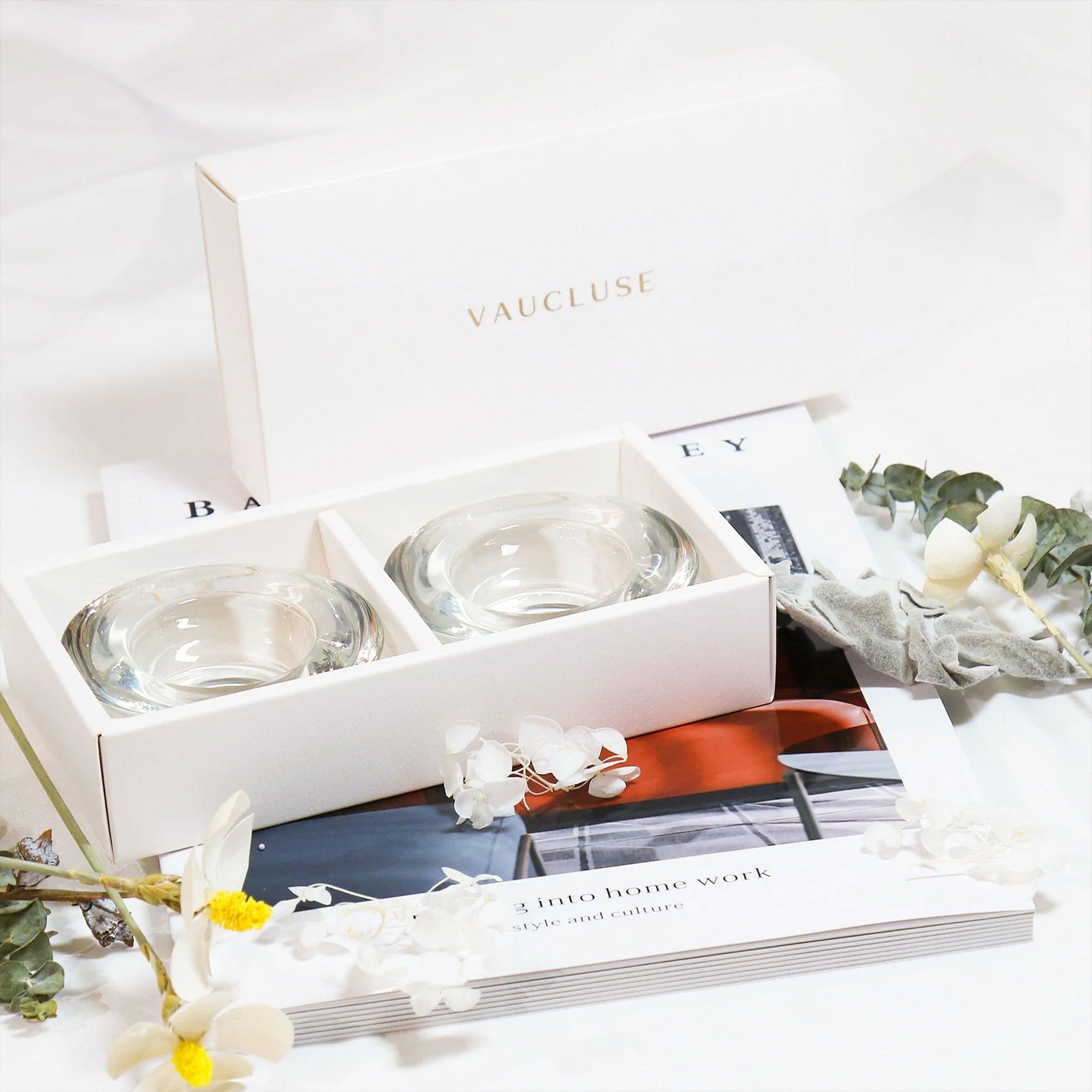 Stylized lifestyle flat lay showing the premium white Vaucluse candle holder gift box paired with elegant white flowers and an open lifestyle magazine.
