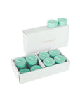 An open luxury white Vaucluse gift box showcasing a premium 16-pack set of light teal ocean scented tealight candles.