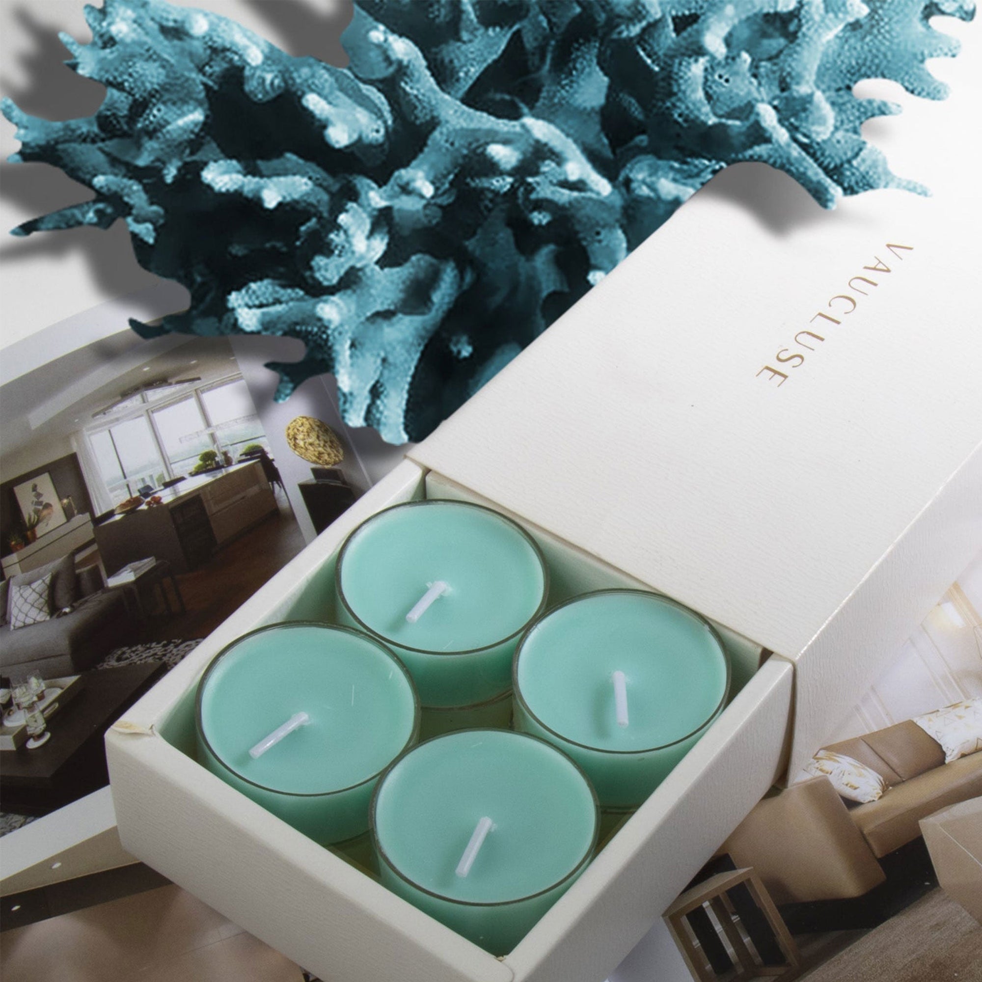 Four unlit light teal ocean scented tealight candles nestled inside a white branded Vaucluse gift box styled with deep blue coral texture in the background.