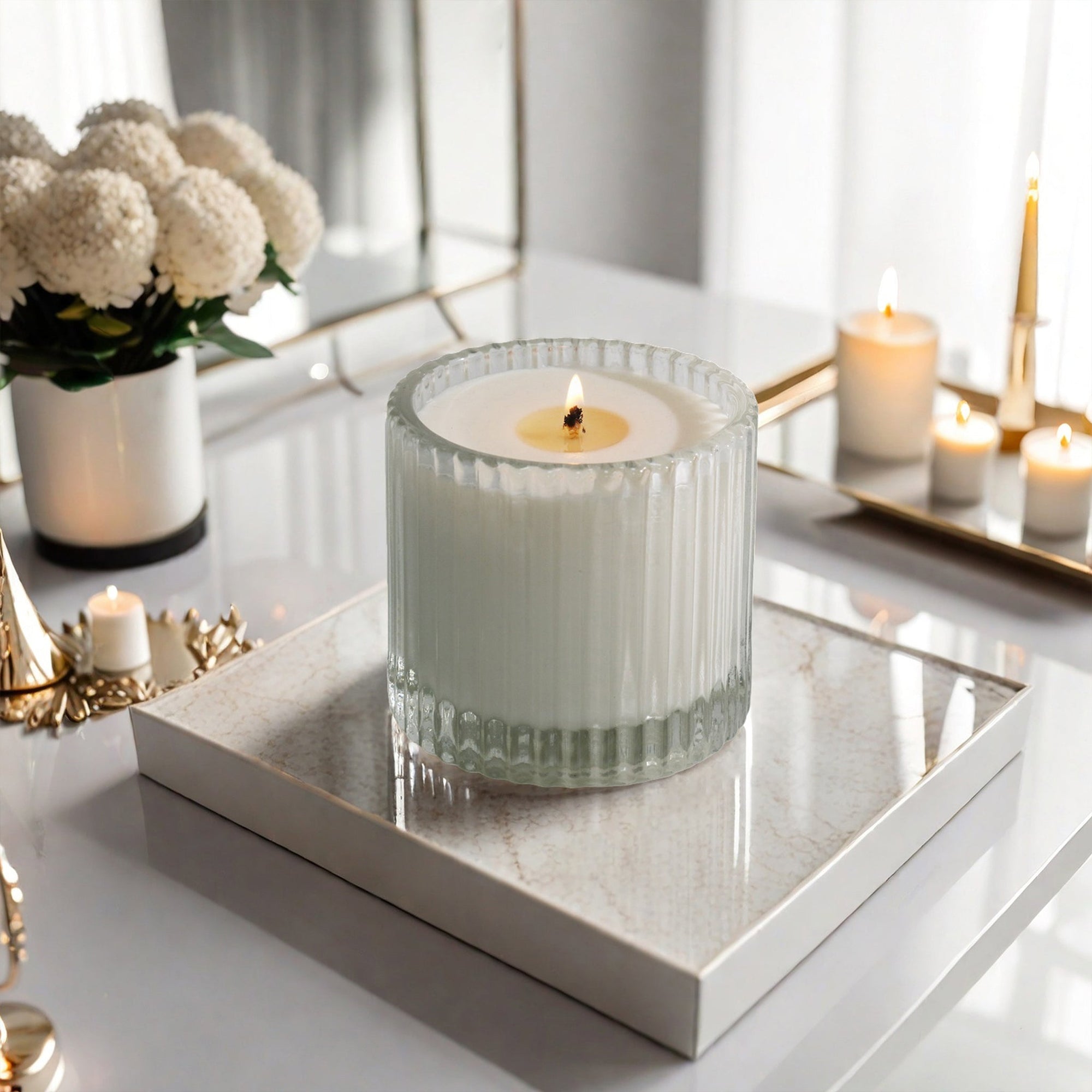 A lit Vaucluse Pear & Freesia luxury scented candle in a ribbed glass jar, placed on a white marble tray in a bright, modern room.