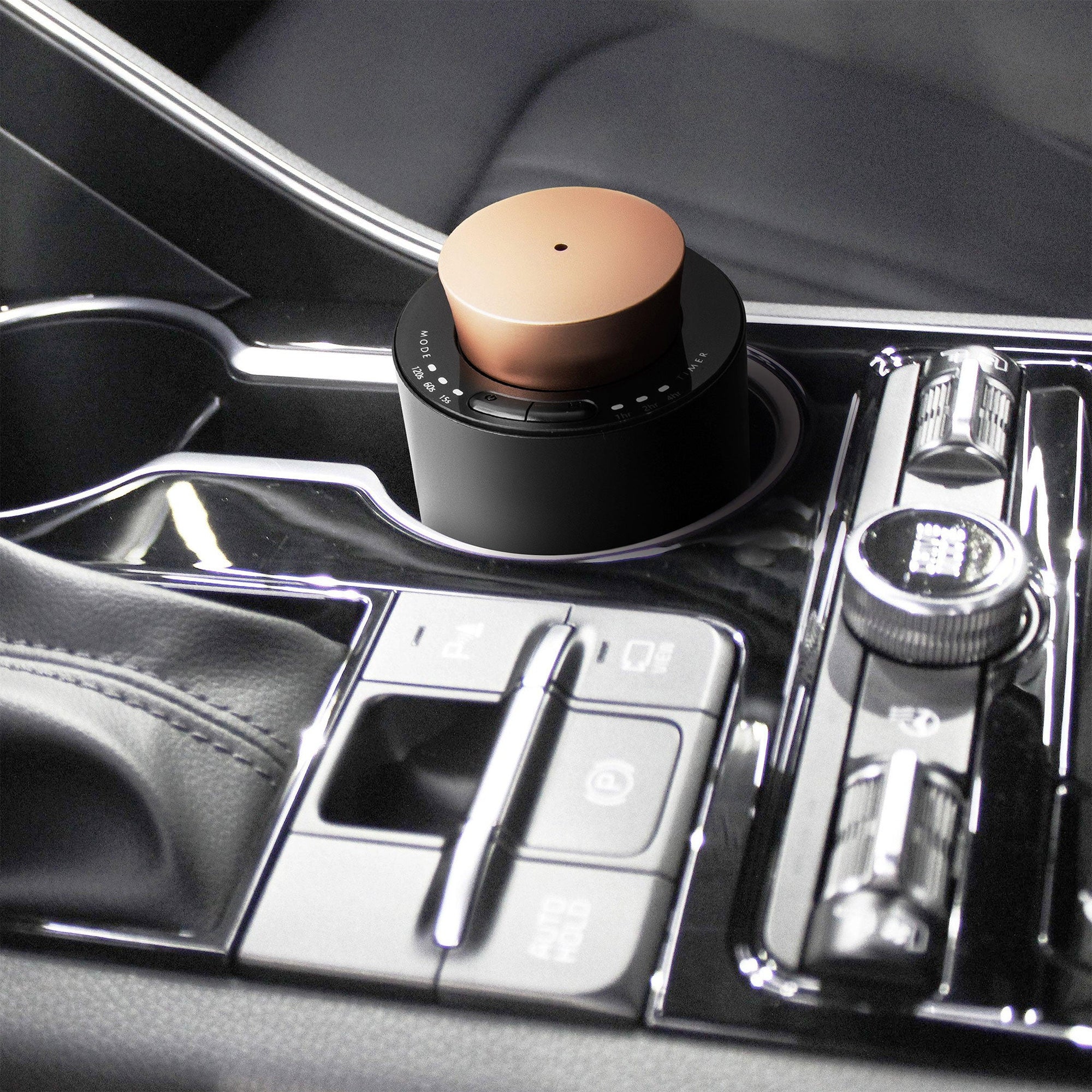 A portable black and rose gold electronic diffuser sitting securely in the center console cup holder of a luxury car interior.