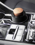 A portable black and rose gold electronic diffuser sitting securely in the center console cup holder of a luxury car interior.