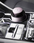 A portable purple dusk electronic diffuser positioned securely in a modern vehicle’s center console cup holder for car aromatherapy.