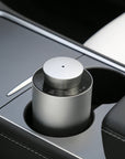 A portable silver electronic diffuser fitted neatly inside the center console cup holder of a car for on-the-go aromatherapy.