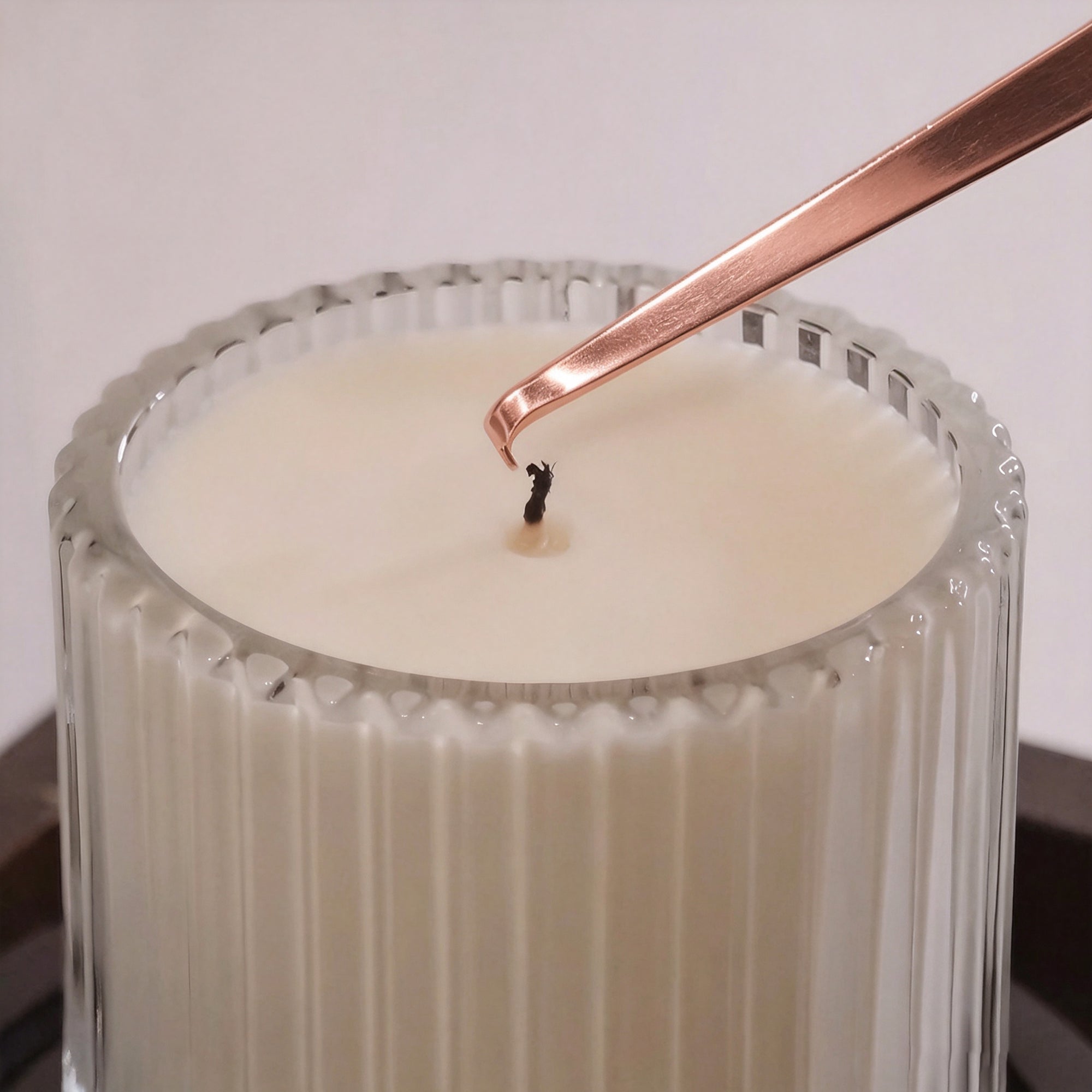 Rose gold candle wick dipper to adjust the wick of a luxury scented candle in a ribbed glass container.