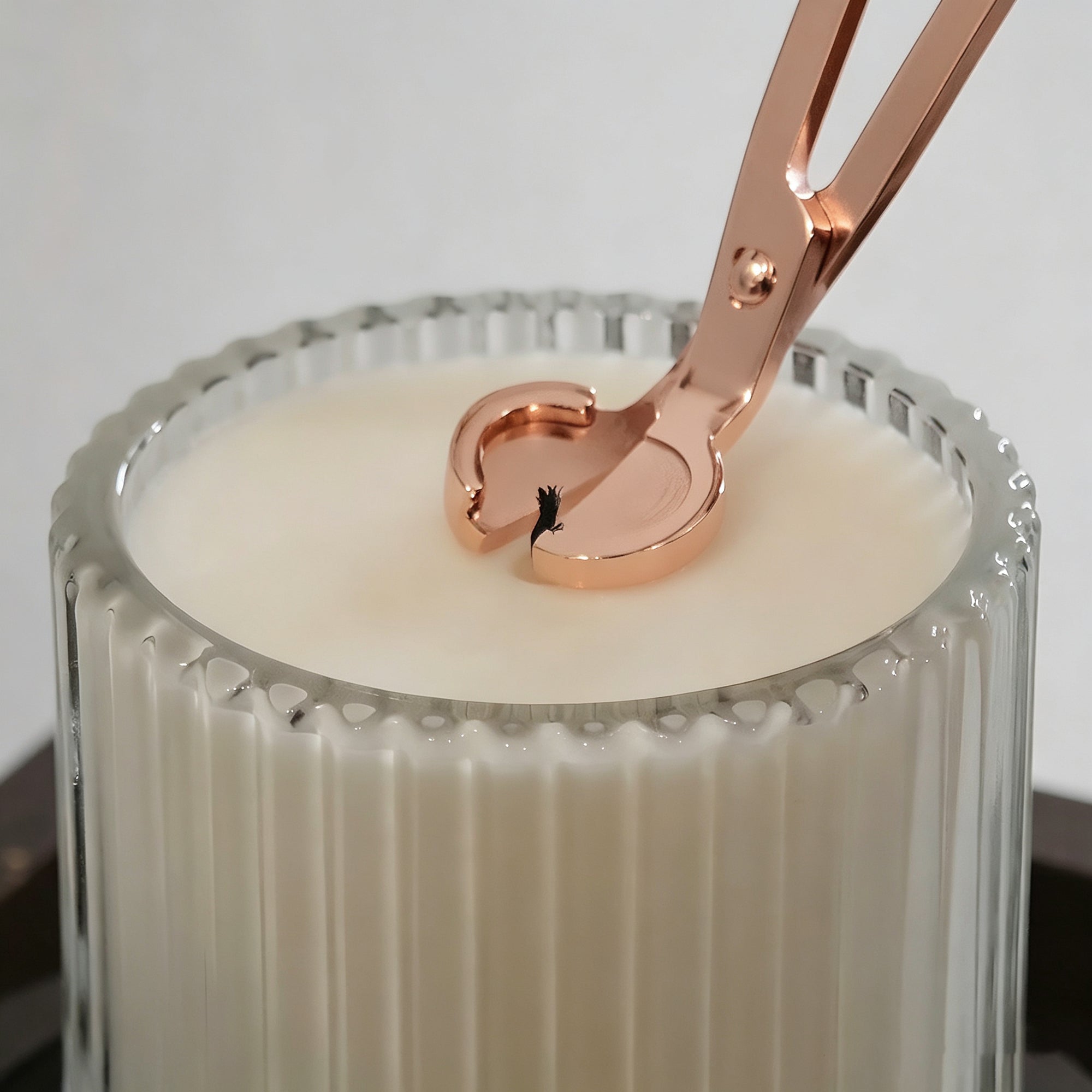 Trimming a candle wick with rose gold wick trimmer scissors before lighting a luxury wax candle.