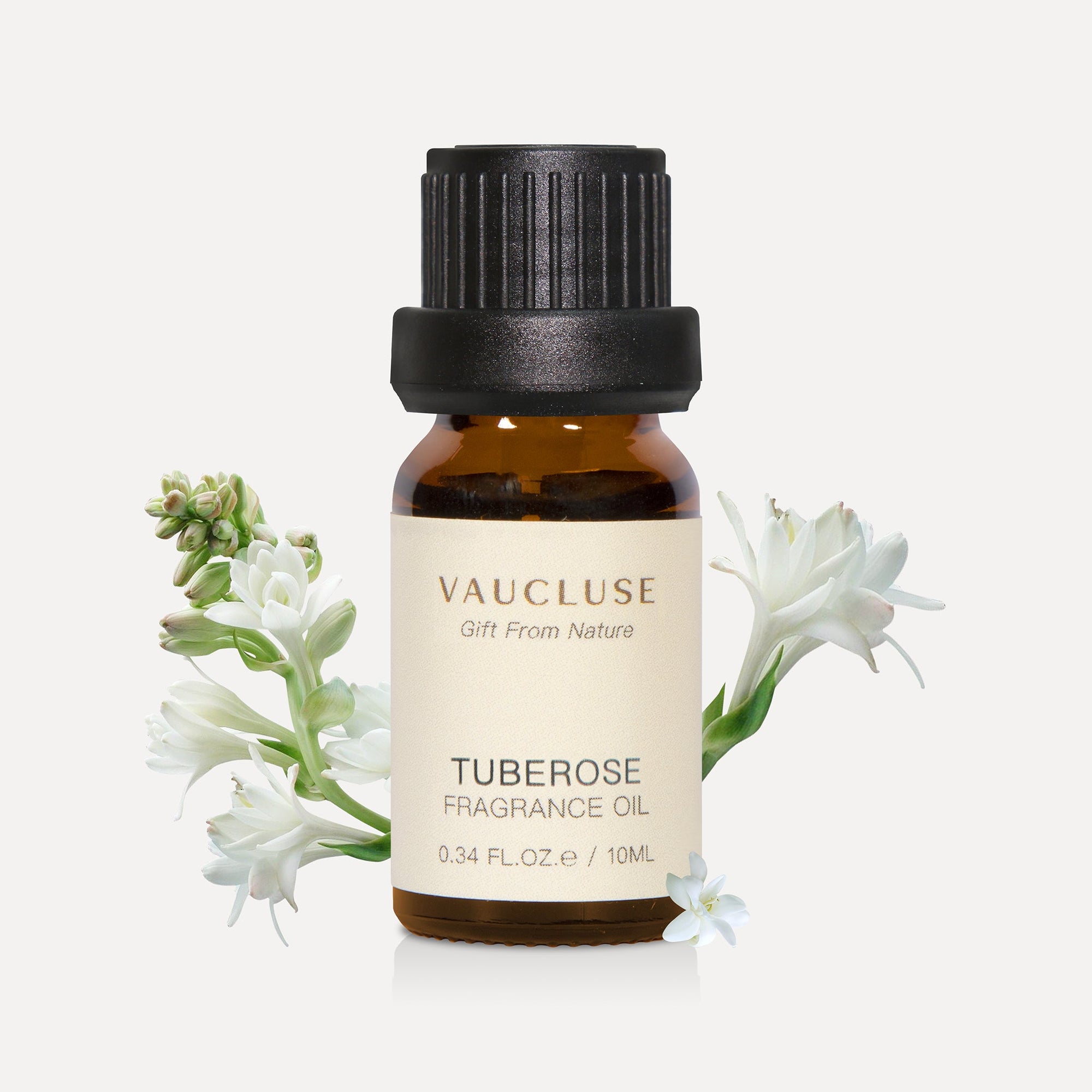 A 10ml amber glass bottle of Vaucluse Tuberose Essential Oil, accented by elegant white tuberose flower blossoms and green stems.