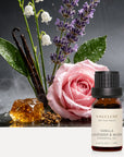 Vaucluse Vanilla Lavender and Musk essential oil bottle against a backdrop of fresh roses, lily of the valley, lavender, vanilla, and amber.