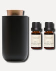 Two 10ml bottles of Vaucluse Vanilla Lavender and Musk essential oil set beside a sleek black electric diffuser.