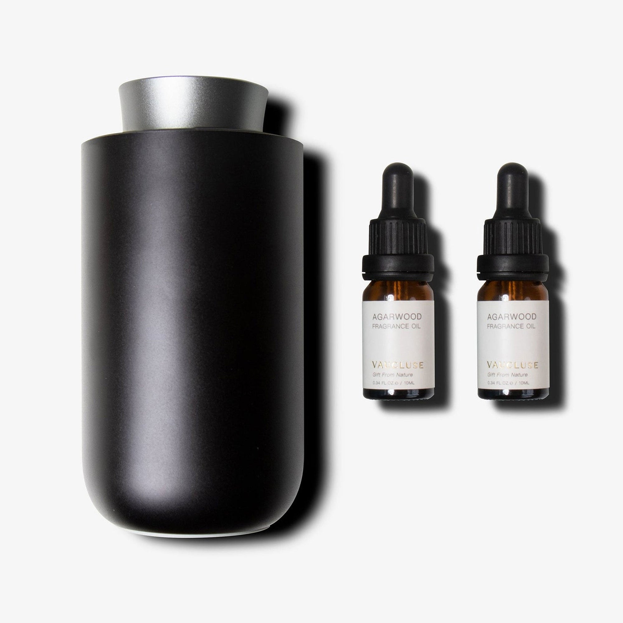 A sleek black and silver waterless nebulizing diffuser standing next to two amber glass essential oil bottles with black droppers.