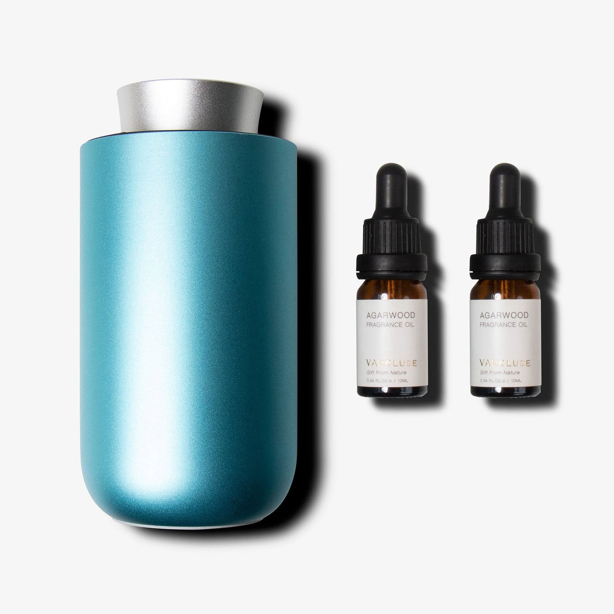 A sleek teal and silver waterless nebulizing diffuser standing next to two amber glass essential oil bottles with black droppers.