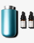 A sleek teal and silver waterless nebulizing diffuser standing next to two amber glass essential oil bottles with black droppers.