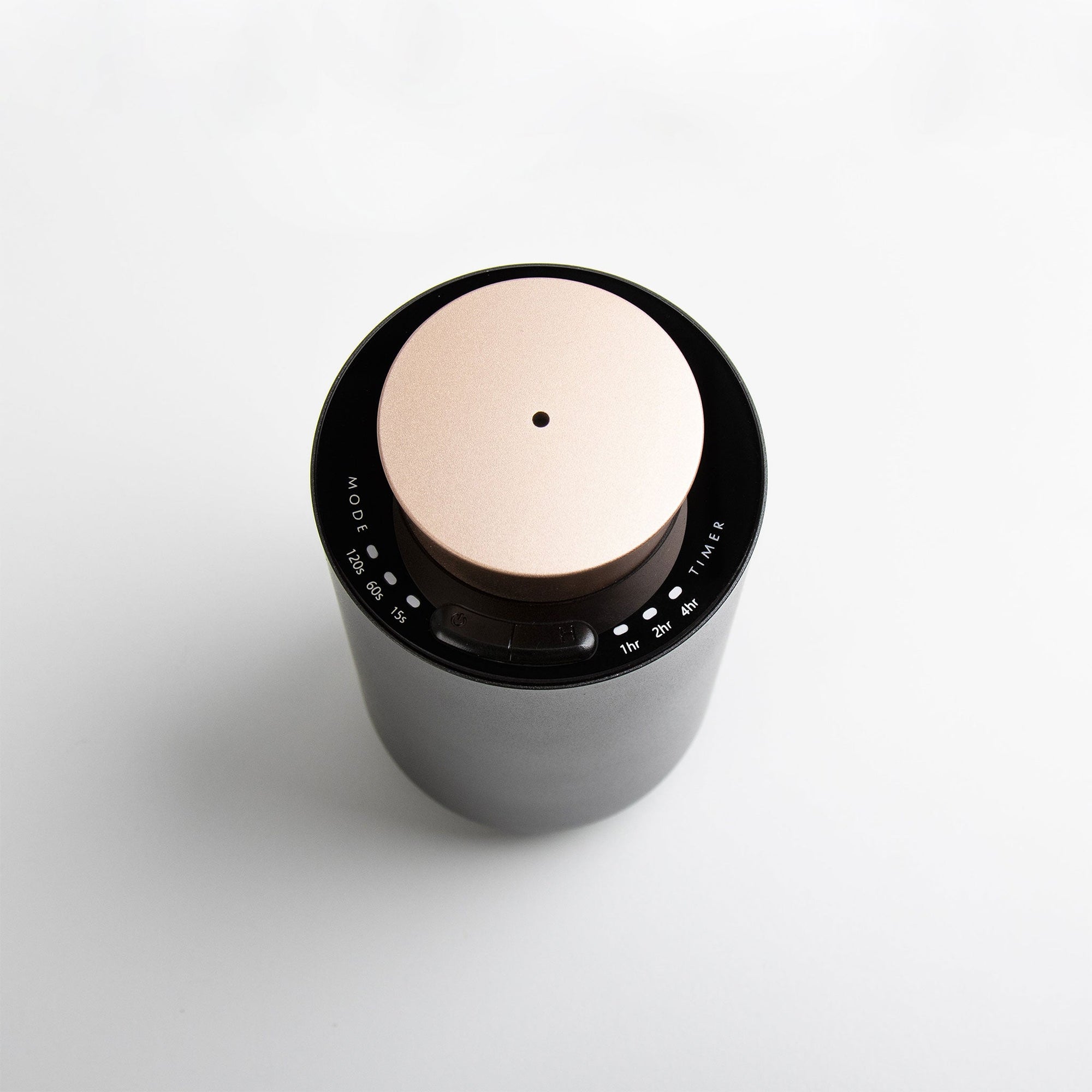 An overhead top-down view of the round black and rose gold waterless diffuser, showing the central mist port nozzle and touch setting indicators.