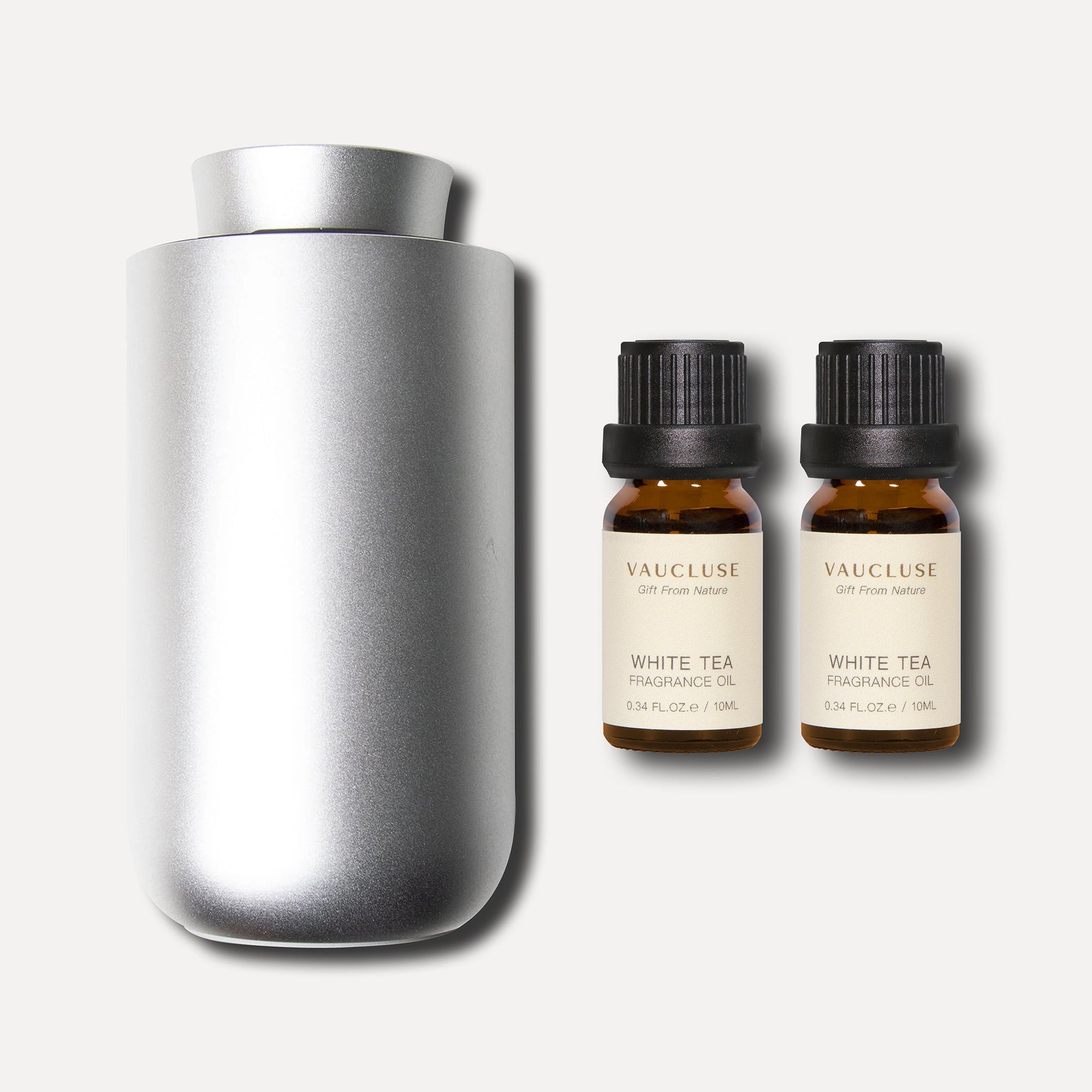 A minimalist silver waterless nebulizing diffuser presented next to a pair of 10ml amber bottles of white tea essential oil.