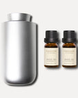 A minimalist silver waterless nebulizing diffuser presented next to a pair of 10ml amber bottles of white tea essential oil.