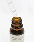 A detailed close-up shot of a glass pipette dropper collecting clear liquid at the open rim of an amber essential oil bottle.