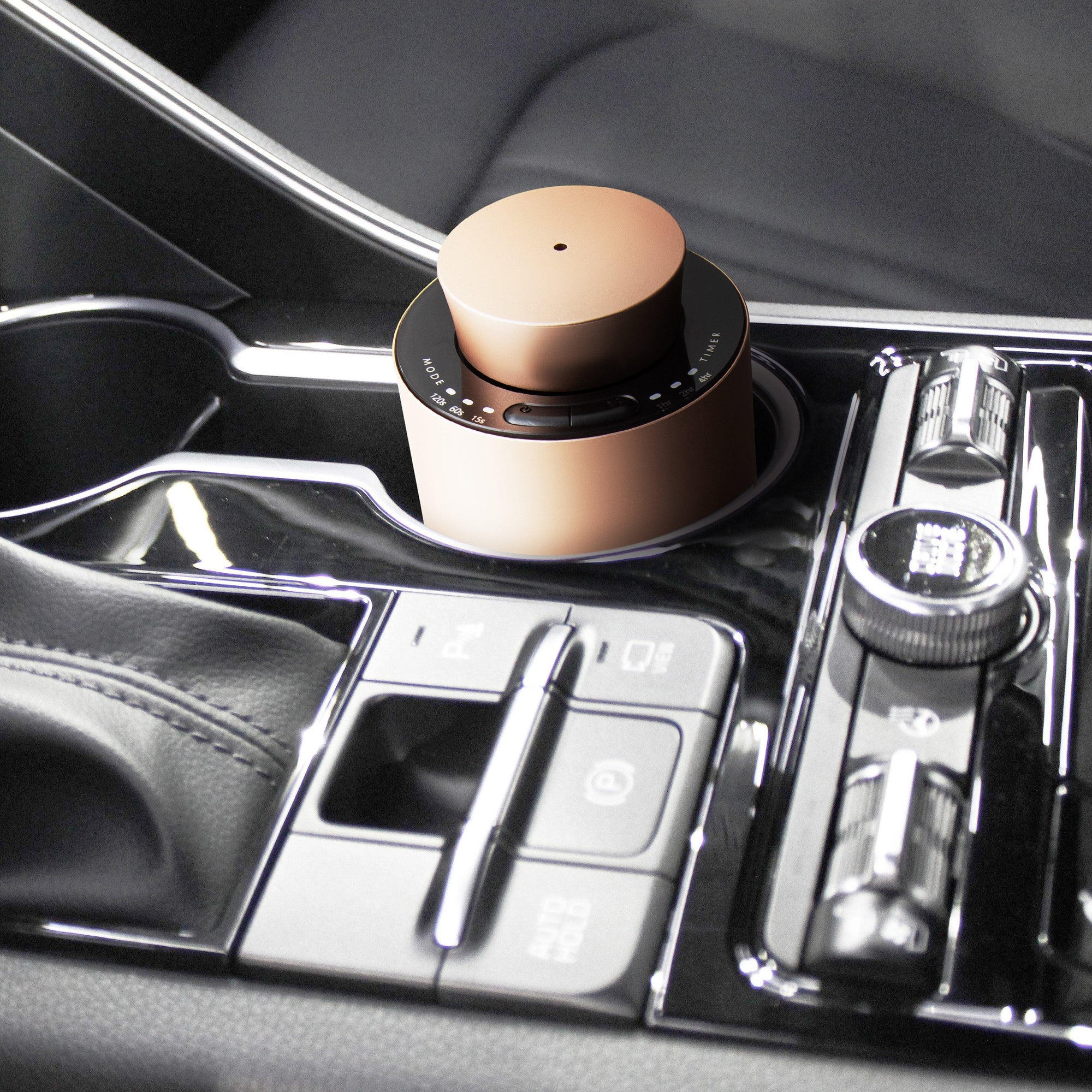 A compact rose gold electronic diffuser fitting perfectly inside a luxury car console cup holder near the gear shift and dashboard controls.