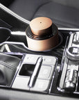A compact rose gold electronic diffuser fitting perfectly inside a luxury car console cup holder near the gear shift and dashboard controls.